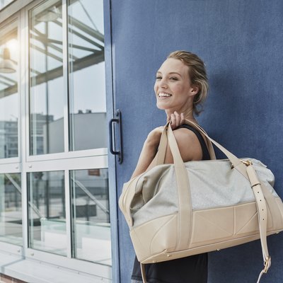 Portrait of smiling young woman with sports bag in front of gym