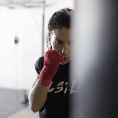 Tough, focused female boxer training at punching bag in gym