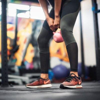 Low Section Of Young Woman Lifting Kettlebell At Gym