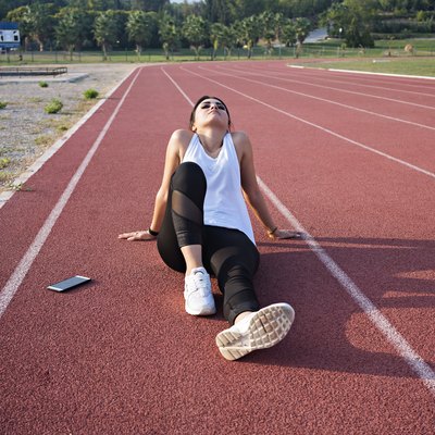 Tired sportswoman lonely sitting in middle of track.