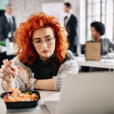 A sad woman eating salad at her desk at work