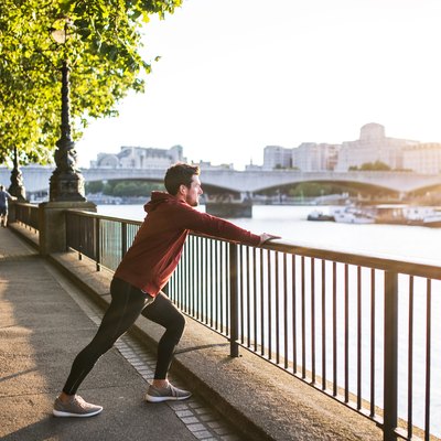 Young sporty man with earphones stretching on a railing outside in a London city.