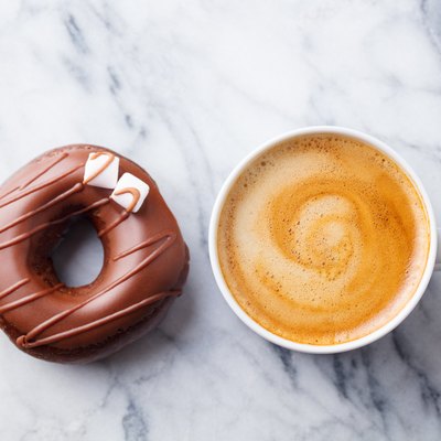 Coffee with chocolate donut in marble table background. Top view.