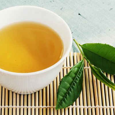 Tea bowl and tea leaves on bamboo mat, close-up