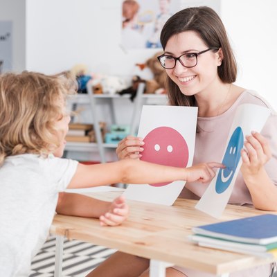 Smiling counselor holding pictures during meeting with young patient with autism