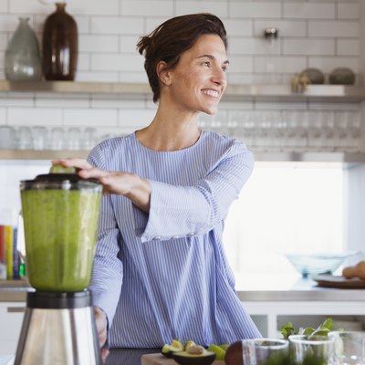 A smiling woman making a green smoothie in a blender