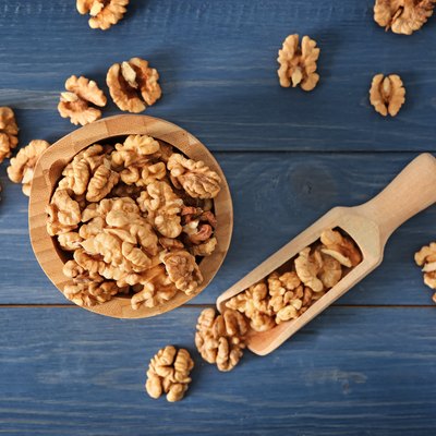 Bowl and scoop with tasty walnuts on color wooden table
