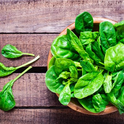 Fresh baby spinach leaves in a bowl on a wooden table.