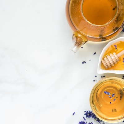 lavender tea in a cup and teapot with honey and fresh flowers over white marble table. herbal drink. top view