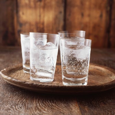 Sparkling water in drinking glass with ice on vintage wooden plate