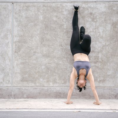 Full Length Of Woman Doing Handstand On Footpath Against Wall