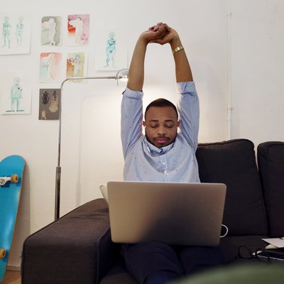Overwhelmed businessman stretching hands while working on laptop in creative office