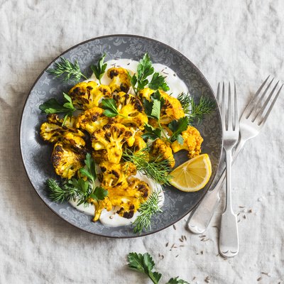 Roasted turmeric cauliflower with greek yogurt dressing. Delicious healthy food on a grey background, top view