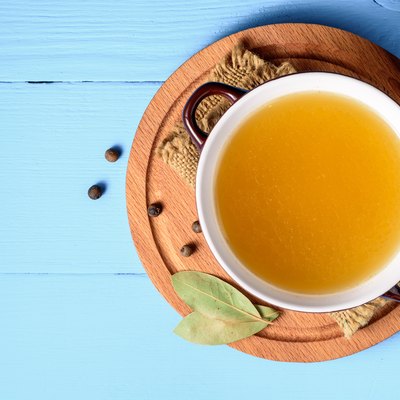 Chicken broth in ceramic bowl on blue wooden background.