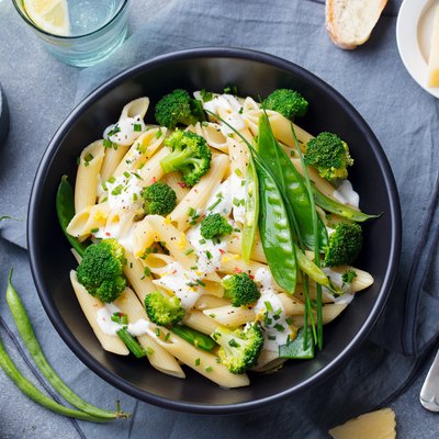 Pasta with green vegetables and creamy sauce in black bowl on grey stone background. Top view.
