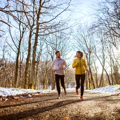 Young sporty happy couple jogging in sportswear through the forest in the sunny winter morning.