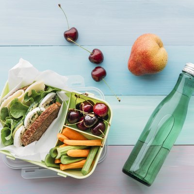 Healthy food in a lunch box, vegetarian sandwich with cheese, lettuce, cucumber, egg and cress, sliced carrot and celery, cherries and pear