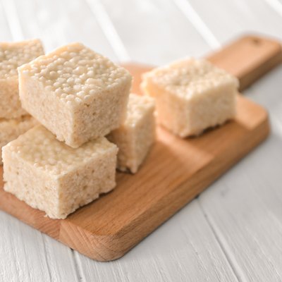 Wooden cutting board with rice treats on white table