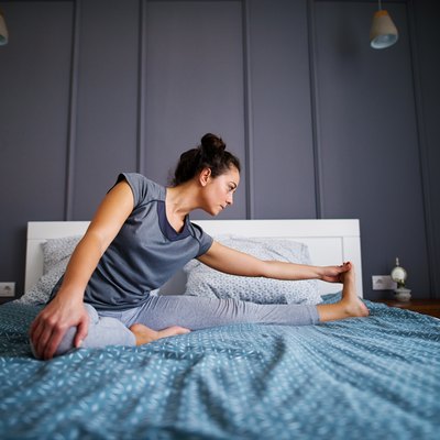 Attractive shape sporty middle aged woman doing seated yoga poses Janu Sirsasana or Head-to-Knee Forward Bend on the bed before sleeping.