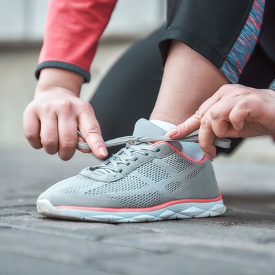 Cropped image of a woman in sports clothing tying shoelace while standing outdoors