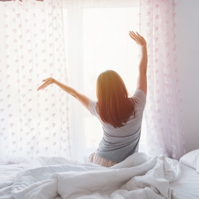 Young asian woman sitting on the bed and stretch oneself in the morning