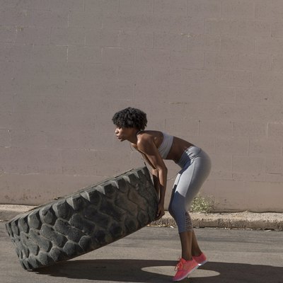Woman lifting tire truck while exercising against wall