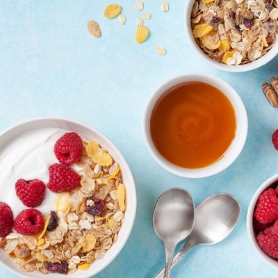 Greek yogurt in bowl with ingredients raspberries, honey and muesli on blue table top view.