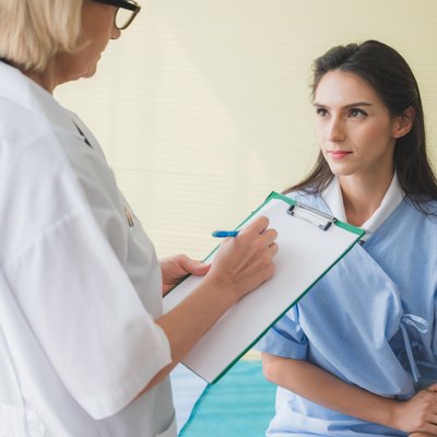 Senior woman doctor and patient discussing and making notes about symptom problem while she sitting on the bed.