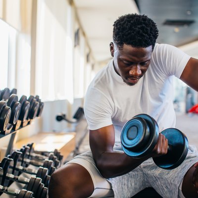 Young man sitting and lifting a dumbbell with the rack at gym