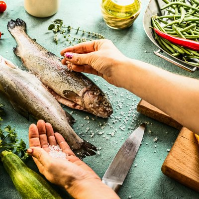 Female woman hands sprinkle with salt raw trout fishes for keto electrolytes