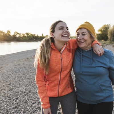 Fit grandmother and granddaughter walking at the river with arms around, having fun