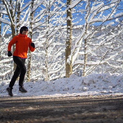 woman jogging on road through snowy winter rural landscape on sunny cold day