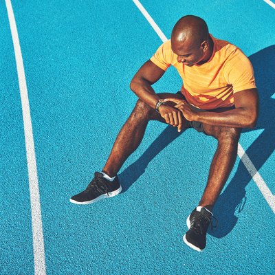 Young athlete sitting on a track checking his running time