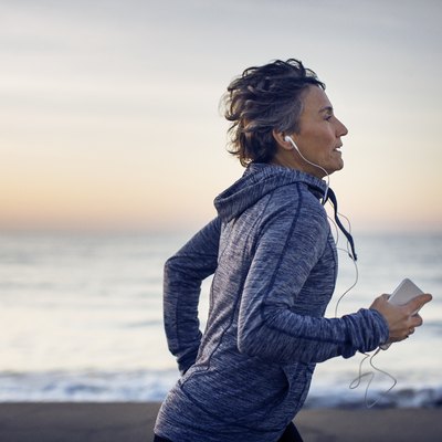Woman jogging while listening music at beach against sky
