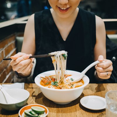 Asian woman eating soup noodles joyfully in restaurant