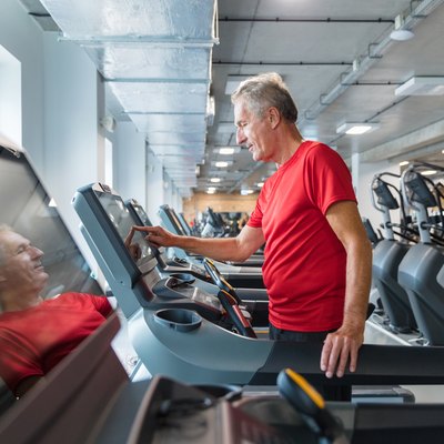 Senior man adjusting speed on treadmill, walking for an hour