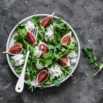 Figs, goat cheese, arugula salad on dark background, top view