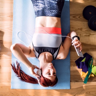 Young fitness woman with smartphone and headphones doing exercise at home.