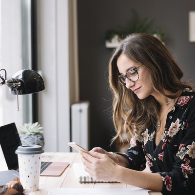 Smiling woman sitting at desk in tattoo studio looking at cell phone