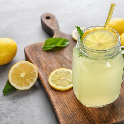Composition with jar of lemon juice and fresh lemons on table