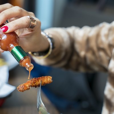 Woman adding hot sauces on crispy, crunchy fried chicken. Fast food