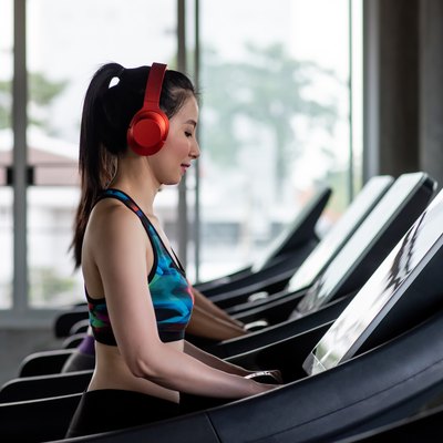 Side View Of Young Woman Wearing Red Headphones While Exercising On Treadmill In Gym