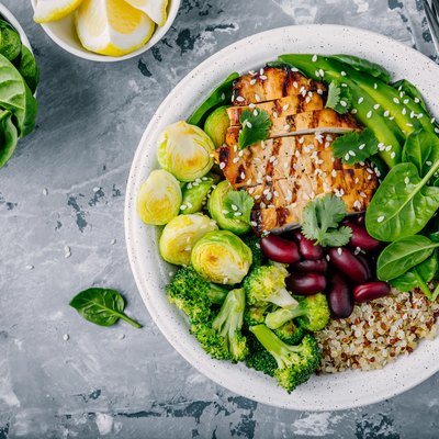 Healthy buddha bowl lunch with grilled chicken, quinoa, spinach, avocado, brussels sprouts, broccoli, red beans with sesame seeds