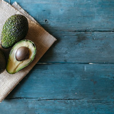 Whole and halved avocado on wooden table