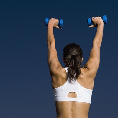 Rear view of mixed race woman holding dumbbells overhead