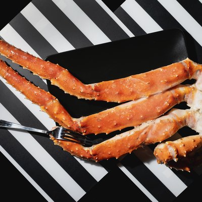 Crab legs and fork in black plate on black and white striped background, view from above