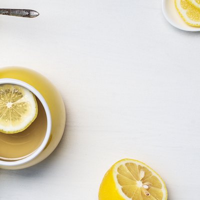 Flat lay of lemon tea in a yellow cup, honey, half a lemon and chamomile on a white background