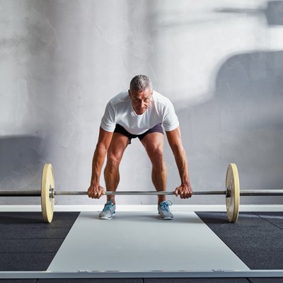 Fit senior man lifting weights alone in a gym