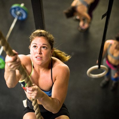 Female athlete performing rope climbing in CrossFit gym