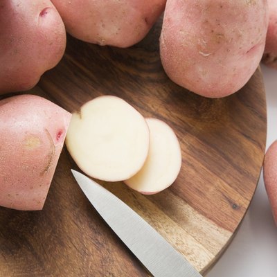 Red potatoes, one partly sliced, on wooden board